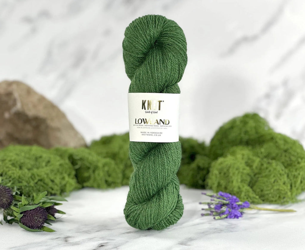 Green skein of yarn with a label on a marble surface with moss and flowers.