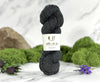 Ball of dark yarn with a label on a marble surface with greenery