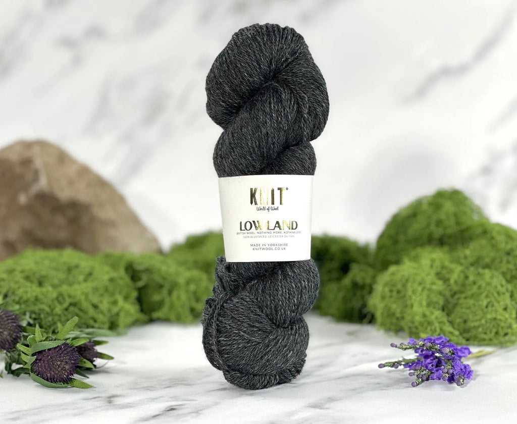 Ball of dark yarn with a label on a marble surface with greenery
