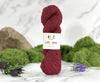 Red skein of yarn with a label on a marble surface surrounded by greenery