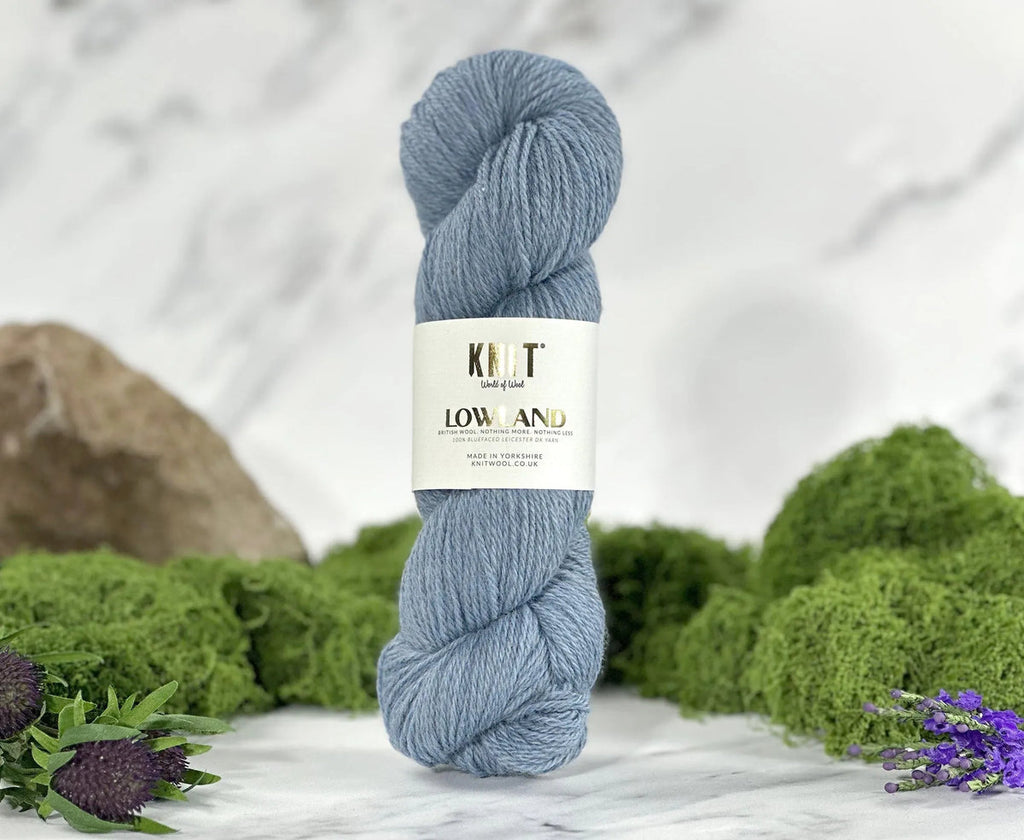 Blue skein of yarn with a label on a white surface with greenery in the background
