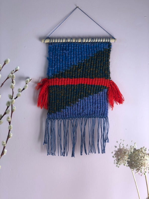 Textile art piece with blue, red, and black colors on a white background
