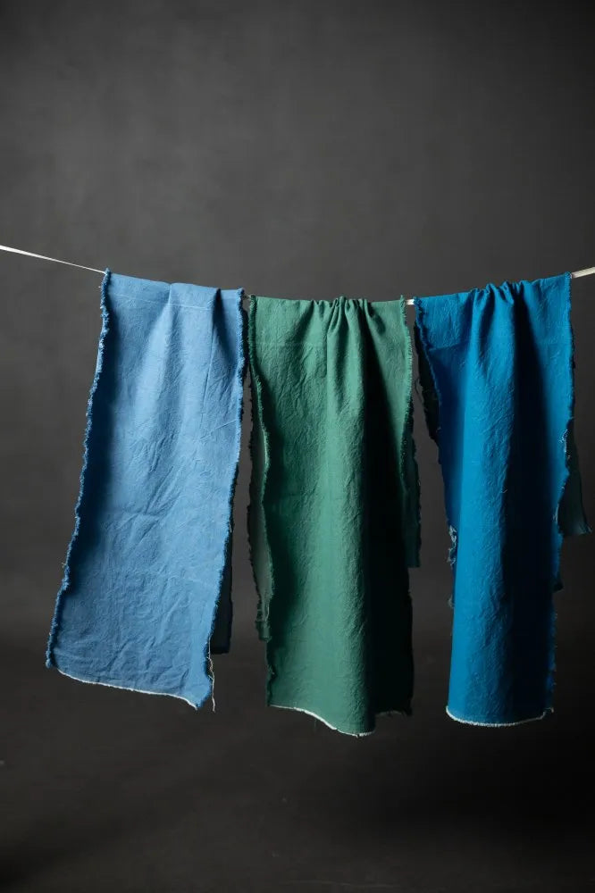 Three pieces of fabric in blue and green hanging on a line against a dark background