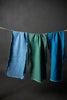 Three pieces of fabric in blue and green hanging on a line against a dark background