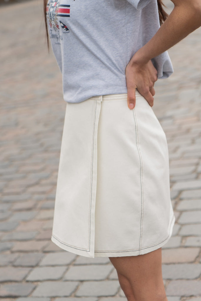 Person wearing a light gray shirt and white skirt on a blurred outdoor background