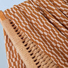 Close-up of a woven chair with a patterned brown and white fabric draped over it against a light blue background.
