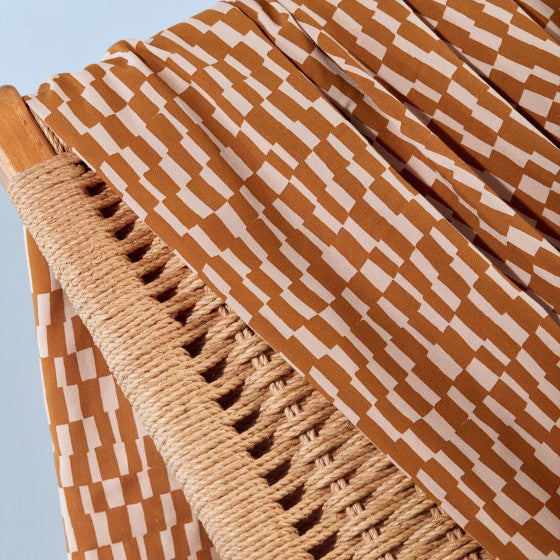 Close-up of a woven chair with a patterned brown and white fabric draped over it against a light blue background.