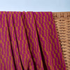 Purple and gold patterned fabric draped over a woven basket against a light blue background