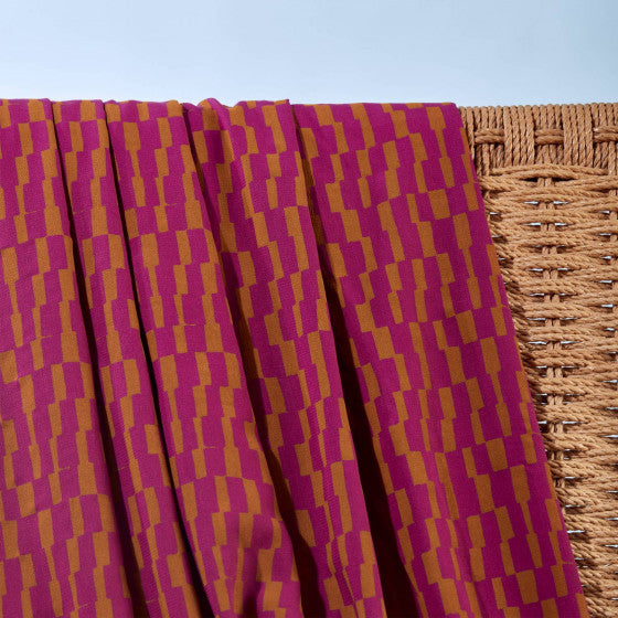 Purple and gold patterned fabric draped over a woven basket against a light blue background