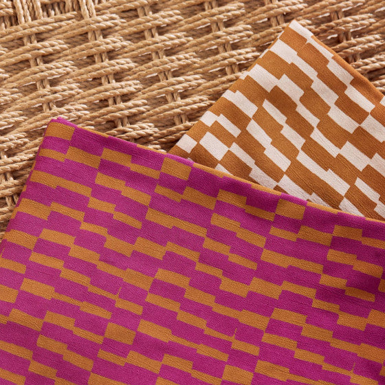 Two pieces of viscose fabric with geometric patterns, one in pink and the other in brown, placed on a woven background.