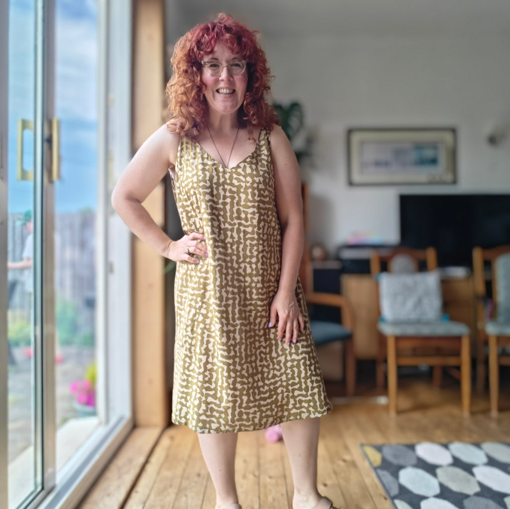 Woman in a patterned dress standing in a room with large windows and furniture.