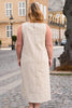 Woman wearing a beige sleeveless dress on a street with buildings in the background