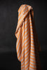 A piece of linen fabric with pastel orange and pale blue/grey wide stripes, draped over a cylindrical object against a dark background.