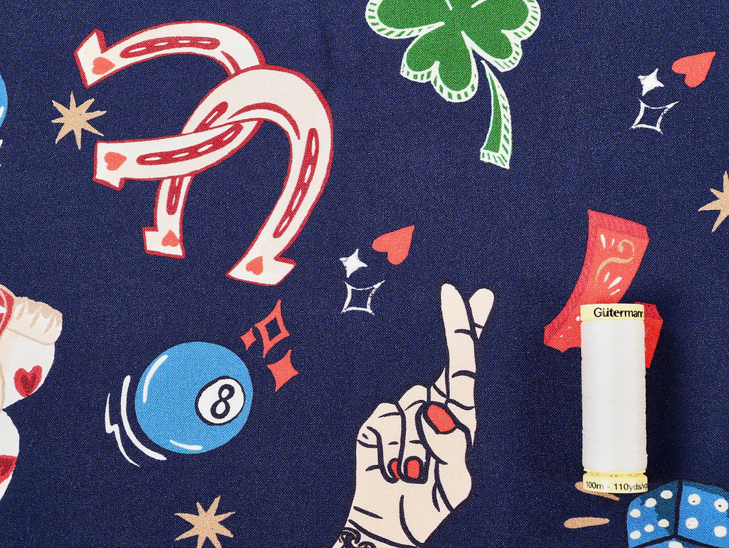 Patterned fabric with various symbols including a horseshoe, dice, and a hand with a cigarette on a blue background.