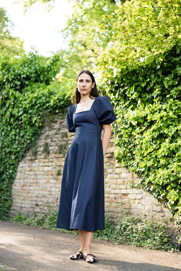 Woman in a navy dress standing in front of a brick wall with greenery