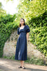 Woman in a navy dress standing in front of a brick wall with greenery