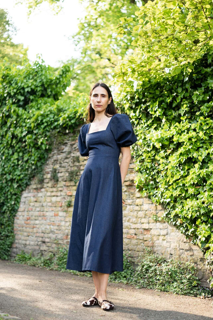 Woman in a navy dress standing in front of a brick wall with greenery