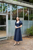 Woman in a navy blue dress standing in front of a greenhouse.