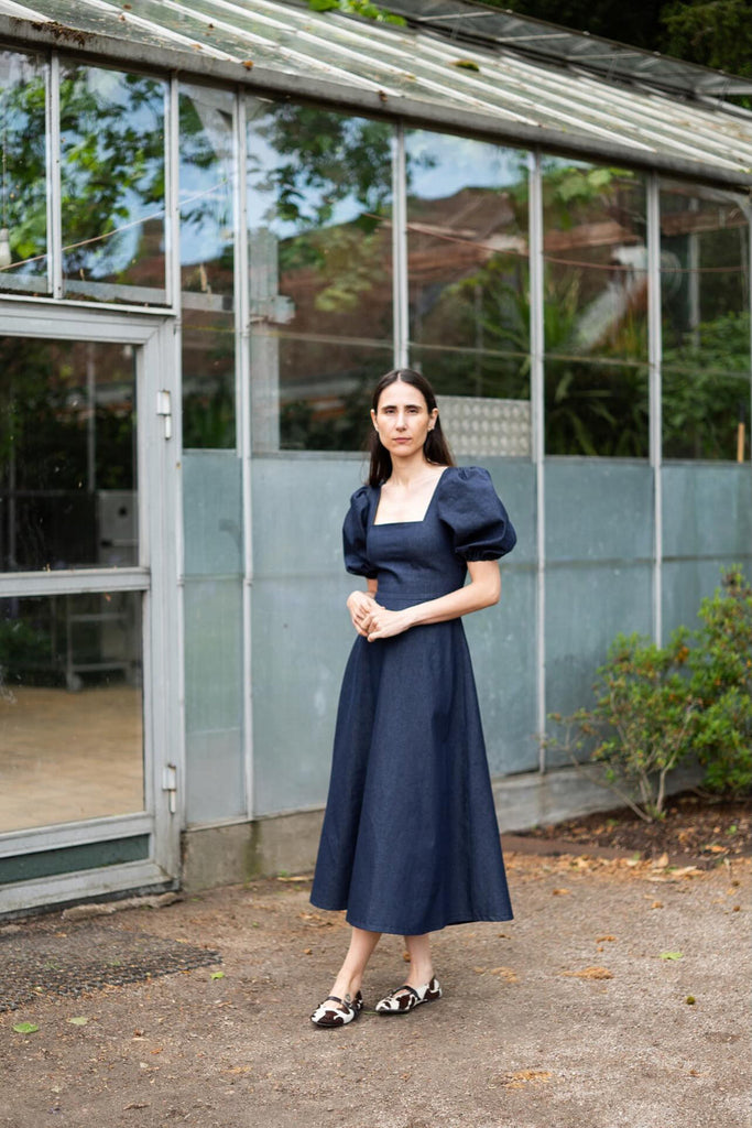 Woman in a navy blue dress standing in front of a greenhouse.