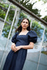 Woman in a navy blue dress standing in front of a glass structure with greenery.