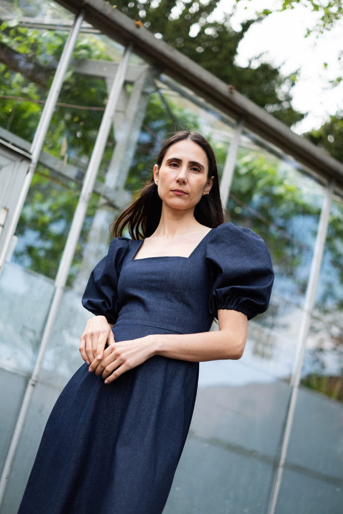 Woman in a navy blue dress standing in front of a glass structure with greenery.