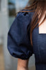 Navy blue dress with puffed sleeves worn by a person, blurred background