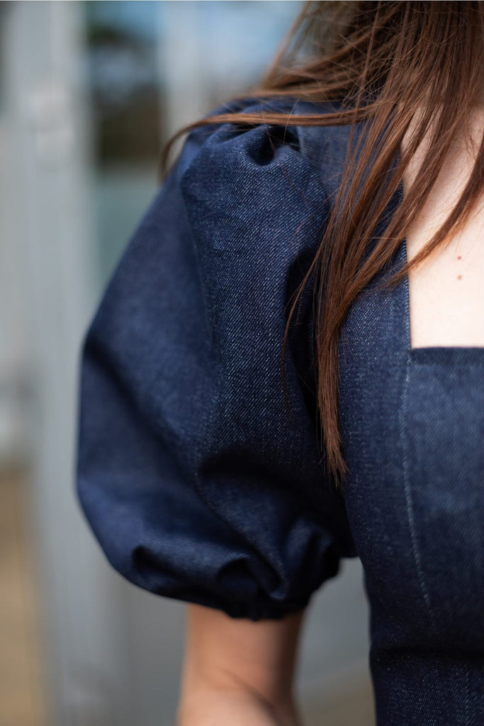 Navy blue dress with puffed sleeves worn by a person, blurred background