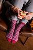Person wearing patterned socks sitting on a chair, holding an apple.