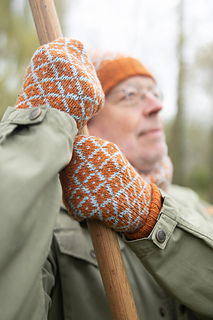 Person wearing orange and white patterned mittens holding a wooden stick outdoors.