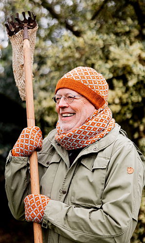 Man wearing an orange knit hat and gloves, holding a rake, with a blurred natural background.