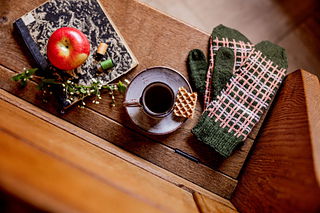 Cozy indoor setting with a cup of coffee, gloves, and an apple on a wooden surface.