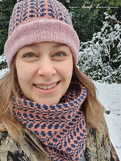 Person wearing a patterned pink and blue hat and scarf in a snowy setting