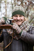 Person holding a vintage camera outdoors with a plaid hat and scarf.