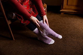 Person wearing purple socks sitting on a wooden floor.