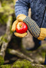 Person holding a red apple with knitted gloves in a natural setting