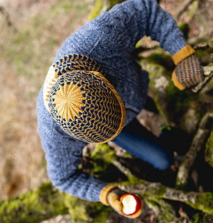 Person wearing a blue knitted sweater and yellow beanie holding a lit candle in a forest setting