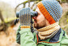 Person wearing a colorful knit hat and gloves using binoculars in a natural setting