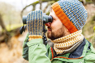 Person wearing a colorful knit hat and gloves using binoculars in a natural setting