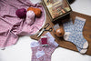 Knitted socks with various patterns on a wooden board with yarn and knitting tools.