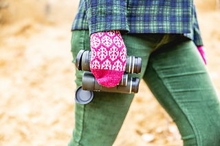 Person wearing a pink knitted glove holding a camera with a blurred natural background