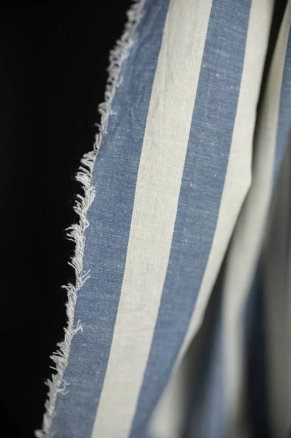 Close-up of blue and white striped fabric with frayed edge on a black background