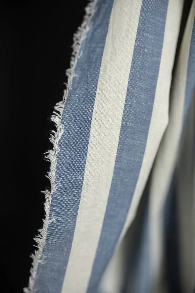 Close-up of blue and white striped fabric with frayed edge on a black background