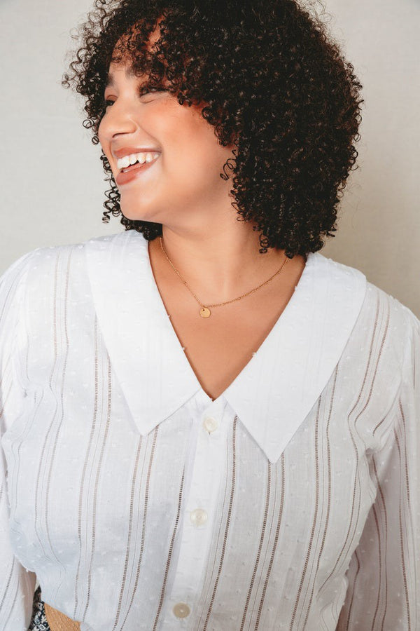 Woman wearing a light-colored blouse with a collar against a neutral background