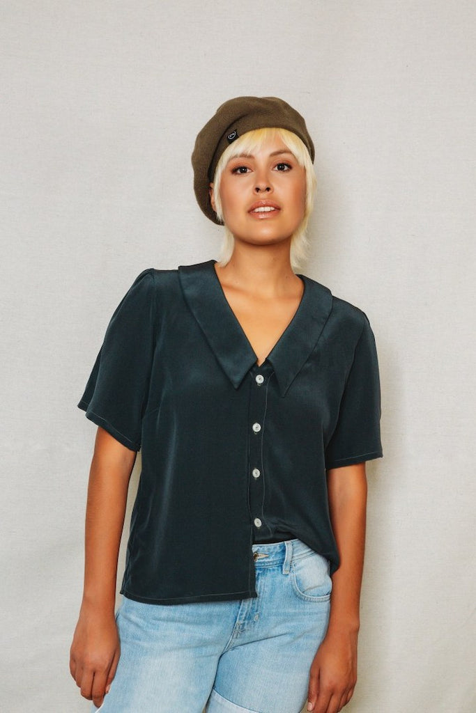 Person wearing a dark green blouse with short sleeves and light blue jeans against a plain background