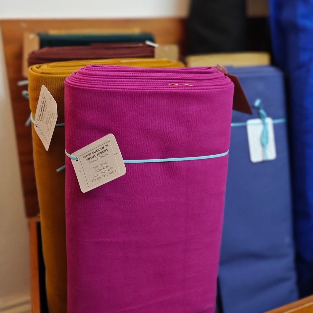 Purple fabric roll with tags on a rack with other fabric colors in the background