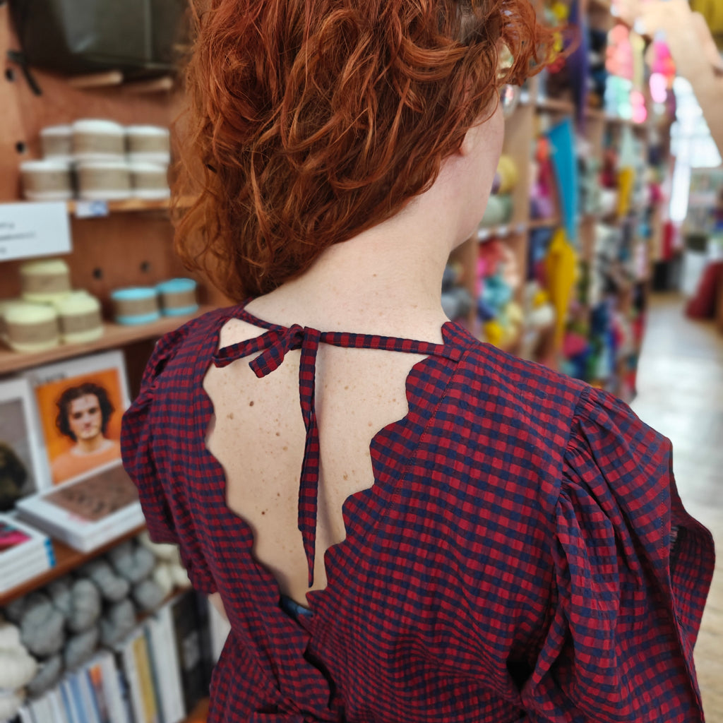 Person wearing a red and black checkered dress with a bow detail in a store setting