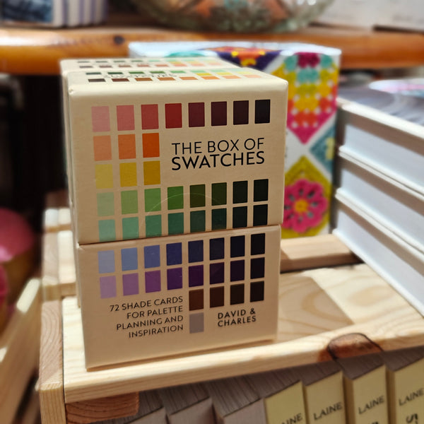 Stack of 'The Box of Swatches' books on a wooden surface with colorful background