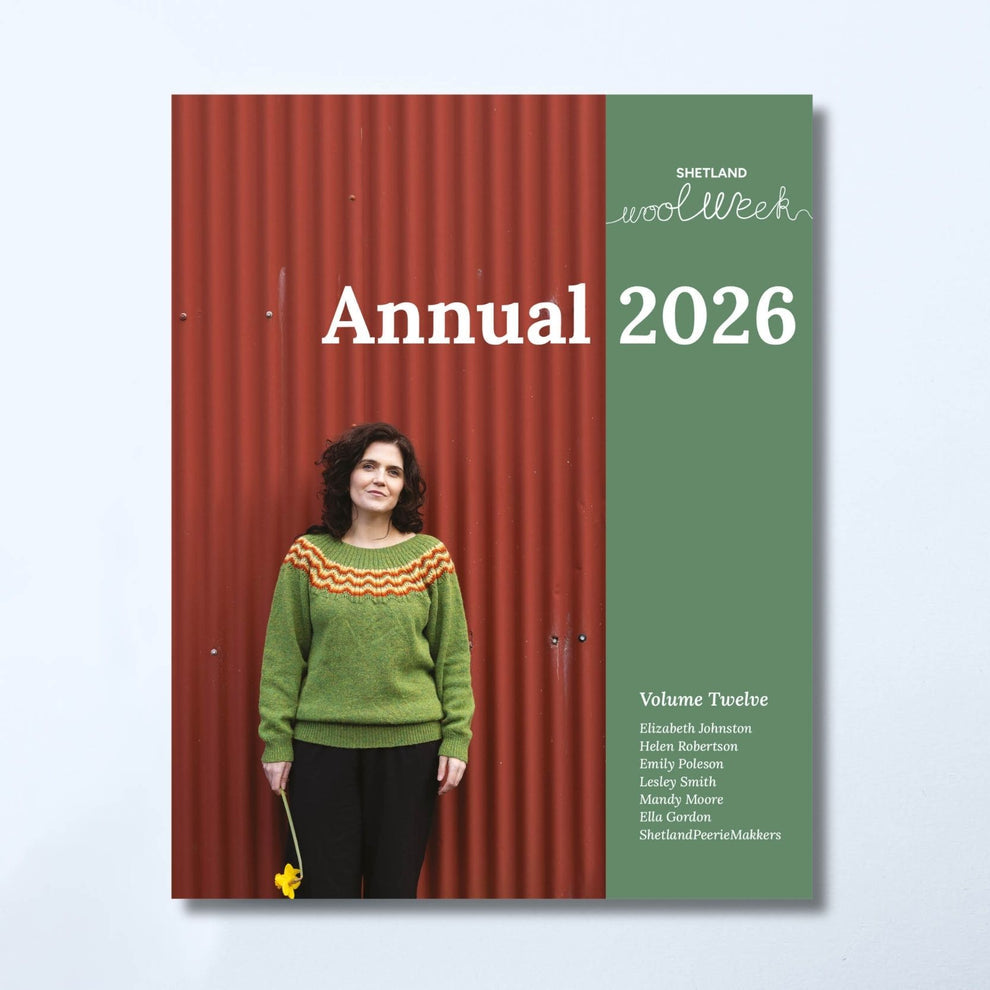 Shetland Wool Week Annual 2026 magazine cover, Volume Twelve, featuring a woman in a green sweater against a red corrugated metal background on the left, and a muted green panel on the right with white text.
