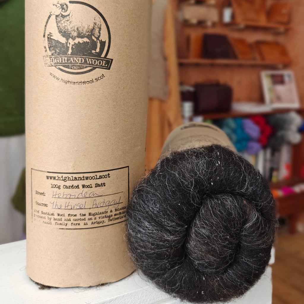 Spool of yarn with a cardboard tube labeled 'Highland Wool' on a wooden surface.