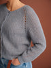 Gray knitted sweater worn by a person on a brown background